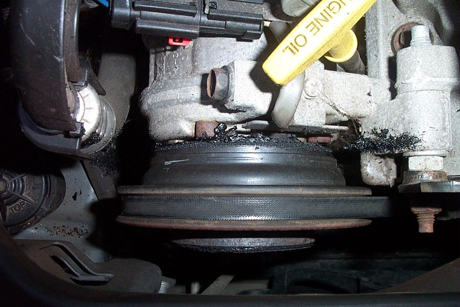 Engine pulley area caked in black shredded belt debris with yellow oil dipstick visible