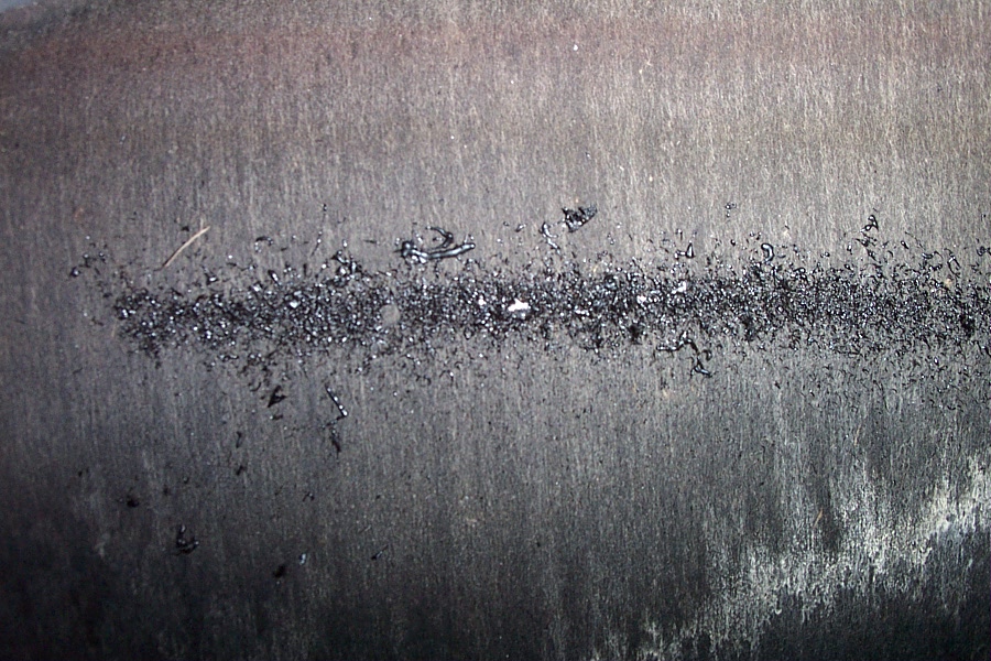 Close-up of a worn brushed metal friction surface with a band of dark debris