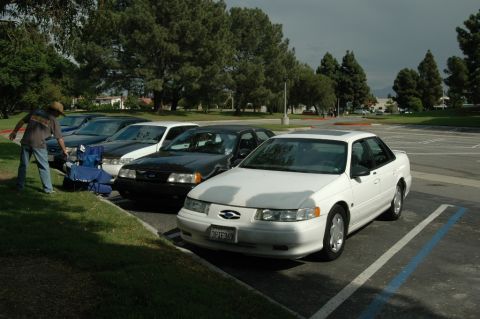 1991 Ford Taurus - Several sedans are parked in a lot, with a man standing near the curb.