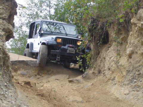1990 Ford Bronco - A white Jeep Wrangler TJ tackles a challenging off-road obstacle on a dirt path.
