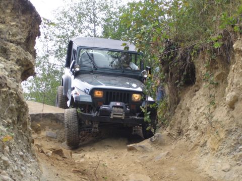 1990 Ford Bronco - Jeep Wrangler tackling a challenging off-road course with steep dirt banks and rocks.