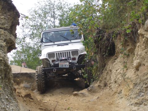 1990 Ford Bronco - A white Jeep Wrangler tackles a challenging off-road trail, its front end visible as it maneuvers through a narrow, rocky passage.