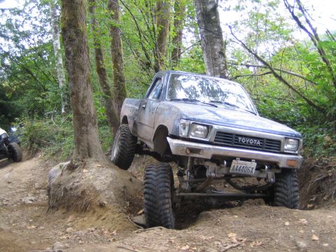 1990 Ford Bronco - Modified Toyota pickup truck tackling a steep, wooded off-road course.