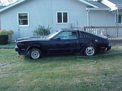 1978 Ford Mustang II - A black 1978 Ford Mustang II coupe sits in a grassy yard next to a house.