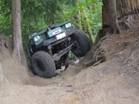 1990 Ford Bronco - A green off-road vehicle navigates a steep dirt incline in a wooded area.