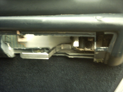 Interior car door latch mechanism, metal and plastic parts, visible spring, dark carpet below