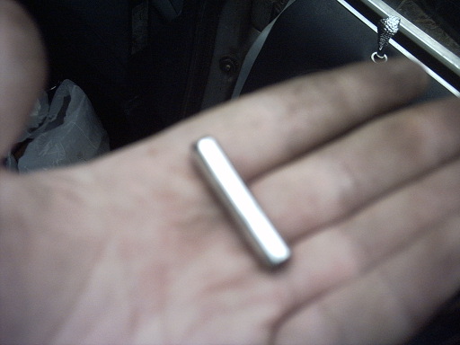 Metal rod held in a palm, with a black fabric bag and part of a car interior visible