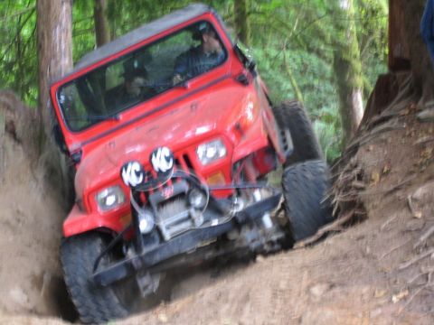 1990 Ford Bronco - This red Jeep Wrangler is navigating a challenging off-road trail, with its tires digging into the dirt.