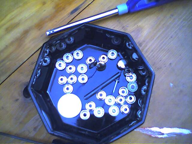 Octagonal black tray with assorted metal fasteners and a screw on a wooden surface