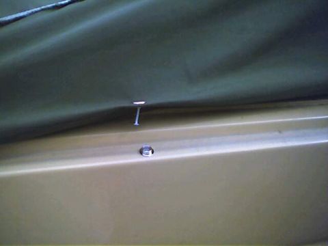1994 Ford Bronco - A nail fastens a dark green soft top to a tan vehicle panel.