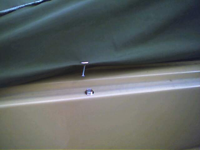 Tan vehicle panel with a nail through a dark green soft top