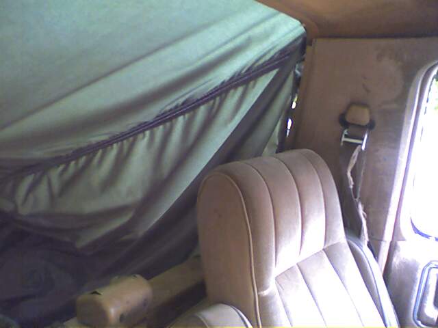 Interior view of a vehicle with a tan seat and a green soft top covering