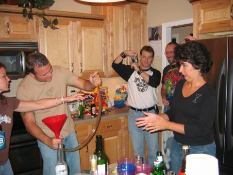 1985 Ford LTD Crown Victoria - A group of people are in a kitchen, with one person pouring a drink using a funnel and tube.