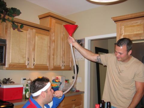 1985 Ford LTD Crown Victoria - Two men are seen participating in a beer funneling activity in a kitchen setting.
