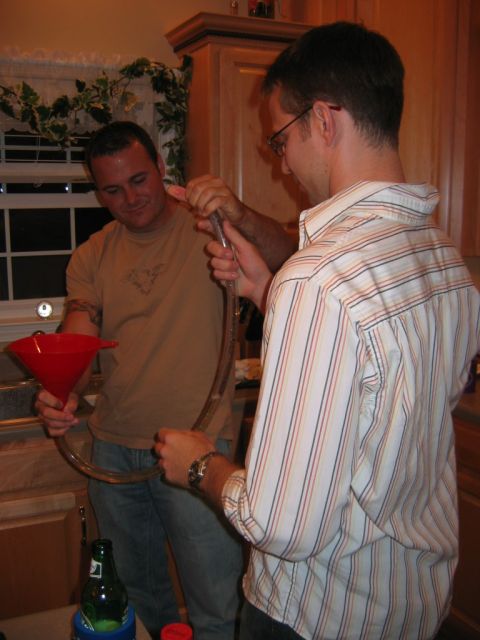 1985 Ford LTD Crown Victoria - Two men are engaged in a party activity involving a beer funnel and tubing in a kitchen setting.