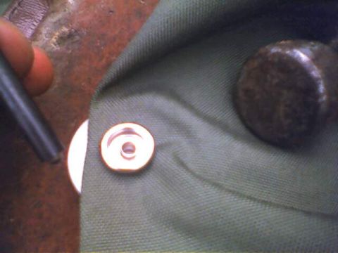 1994 Ford Bronco - A snap fastener is being installed on a piece of green fabric, with a tool and another metal object nearby.