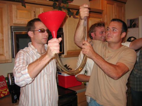 1985 Ford LTD Crown Victoria - Three men are shown participating in a drinking game using a beer funnel in a kitchen setting.