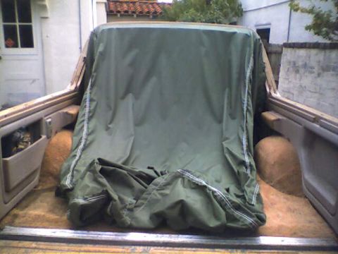 1994 Ford Bronco - The rear interior of a vehicle is mostly obscured by a large green tarp, with some carpeting and side panels visible.