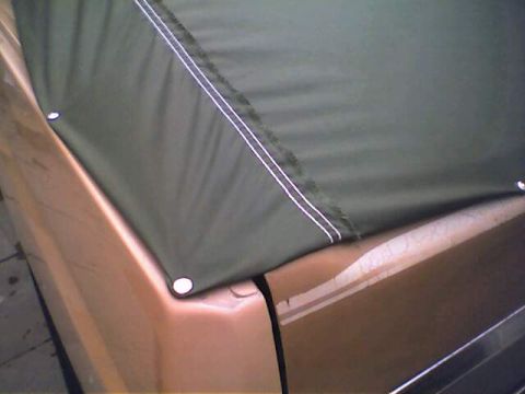1994 Ford Bronco - A close-up view of a green soft top with white stitching, attached to the rear quarter panel of a tan vehicle.