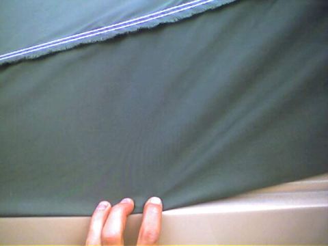 1994 Ford Bronco - A hand is shown pulling on the edge of a dark green fabric, possibly a car's soft top.