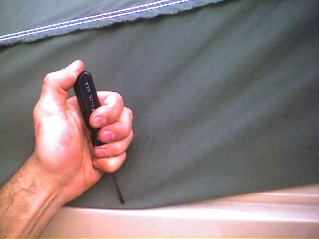 Hand grips a T-15 hex wrench against a dark green fabric background