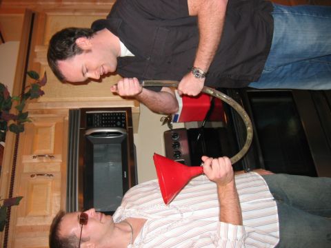 1985 Ford LTD Crown Victoria - Two men are engaged in drinking from a beer bong in what appears to be a kitchen setting.