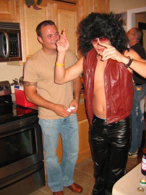 1985 Ford LTD Crown Victoria - Two men are in a kitchen, one dressed in a costume with an afro wig and leather pants.