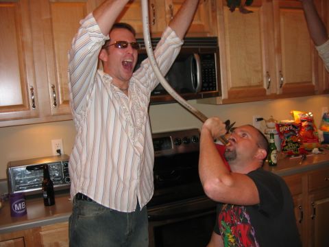 1985 Ford LTD Crown Victoria - Two men are seen drinking from a tube in a kitchen during what appears to be a party.