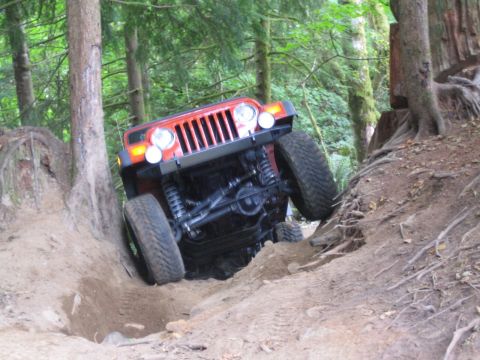1990 Ford Bronco - An orange Jeep Wrangler navigates a challenging off-road trail through a forest.