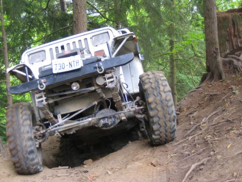 1990 Ford Bronco - This off-road vehicle navigates a steep, muddy incline in a wooded area.