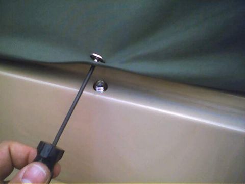 1994 Ford Bronco - A screwdriver is used to attach a soft top to a tan vehicle body.