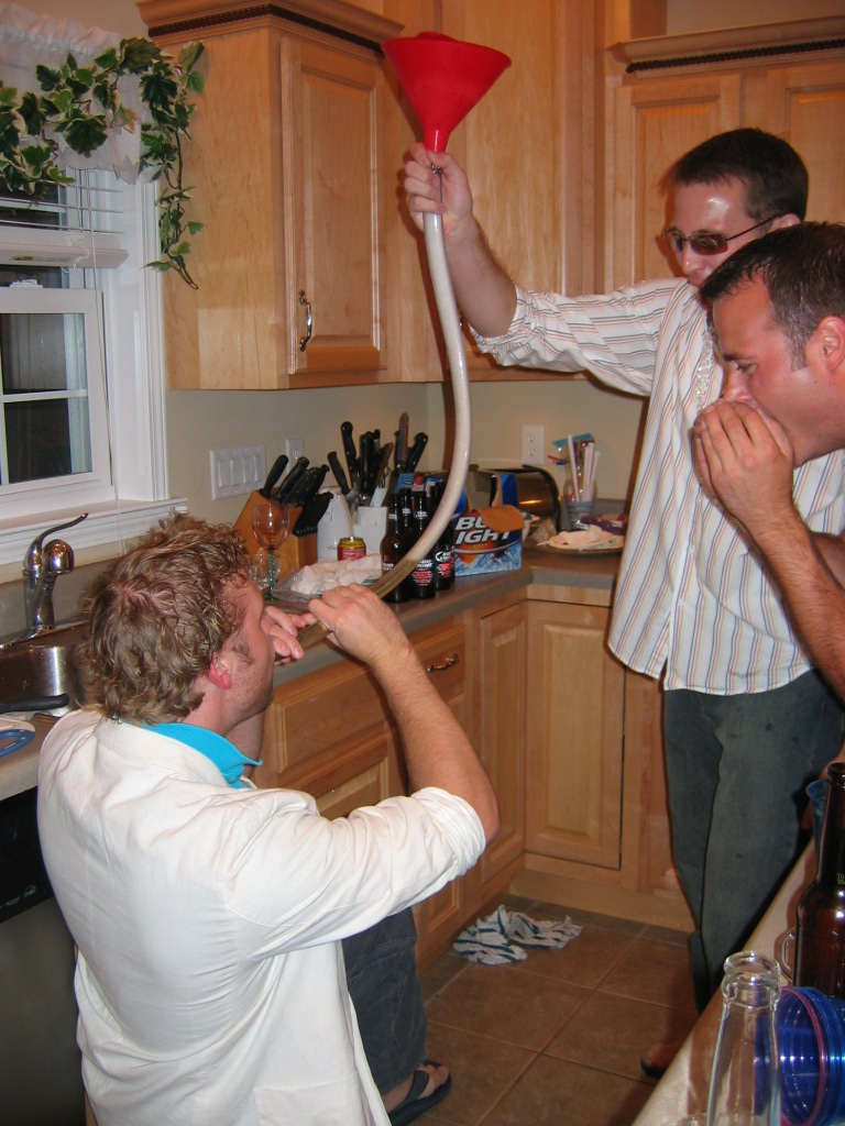 Guys drinking from a beer funnel in a kitchen. One guy is drinking, another is holding the funnel, and a third is watching