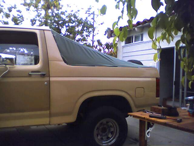 Side view of tan Ford Bronco with green soft top covering the rear. Tools on table nearby