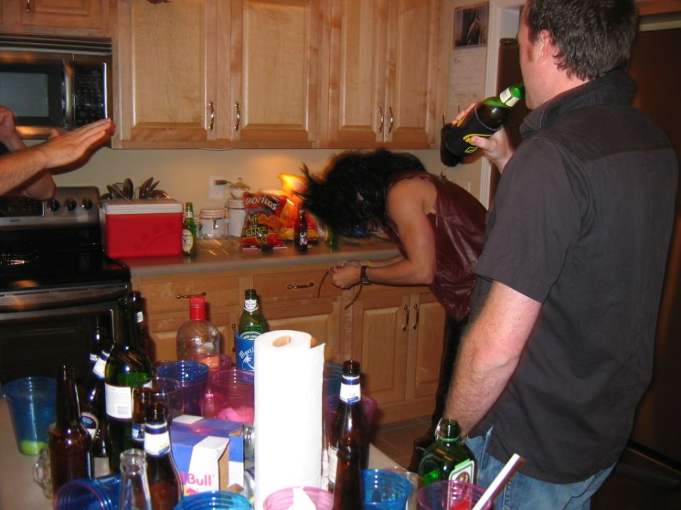 Kitchen counter with bottles, cups, and snacks, two people visible