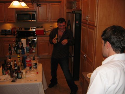 1985 Ford LTD Crown Victoria - A party scene in a kitchen with two men and a table laden with alcoholic beverages.