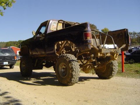 1979 Ford Bronco - Modified pickup truck with custom roll cage and large off-road tires sits parked on a dirt lot.