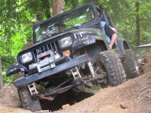 1990 Ford Bronco - Black Jeep Wrangler navigates a challenging off-road trail in a wooded area.