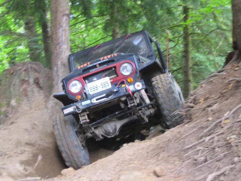 1990 Ford Bronco - This modified off-road vehicle navigates a challenging dirt trail in a forest setting.