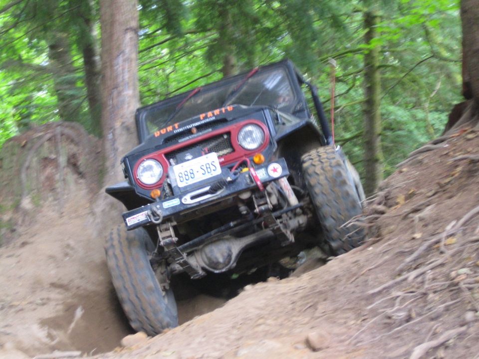 Off-road vehicle with license plate 888-SBS climbing a steep dirt incline in a wooded area