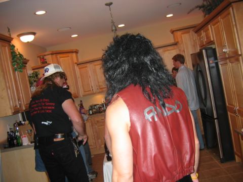 1985 Ford LTD Crown Victoria - Partygoers in a kitchen, one with a mullet wig and red vest, another with a white hat and graphic t-shirt.