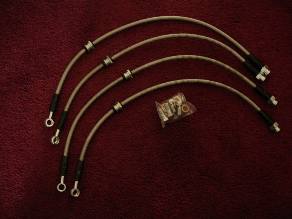 Four braided brake lines with banjo fittings and a bag of assorted fittings on a red textured surface