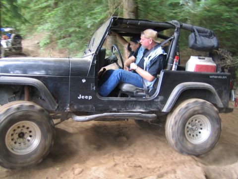 1990 Ford Bronco - A black Jeep Wrangler navigates an off-road trail with two people inside.