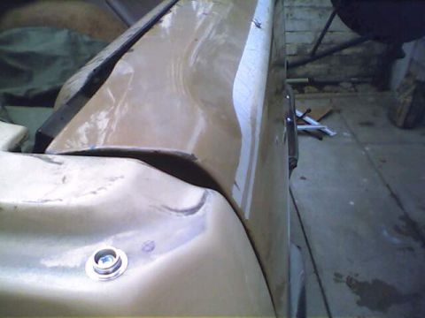 1994 Ford Bronco - Close-up of a damaged tan car body panel with visible repair marks and a silver bolt.