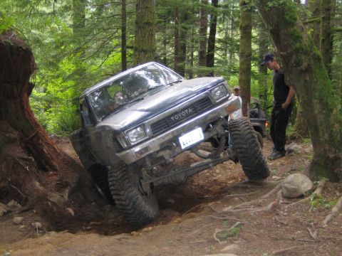 1990 Ford Bronco - A Toyota pickup truck navigates a steep, wooded trail with large tires.