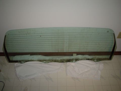1984 Ford Bronco - A detached rear window glass, likely for a vehicle, is shown laid flat on the floor.