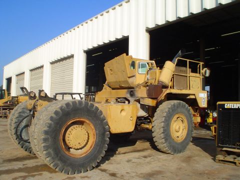 1966 International School Bus - A yellow heavy equipment vehicle is parked in front of a white industrial building with multiple garage doors.