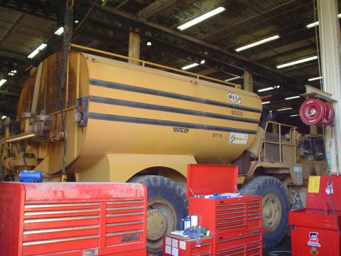 1966 International School Bus - A large yellow industrial vehicle with a tank is parked in a garage, surrounded by red toolboxes.