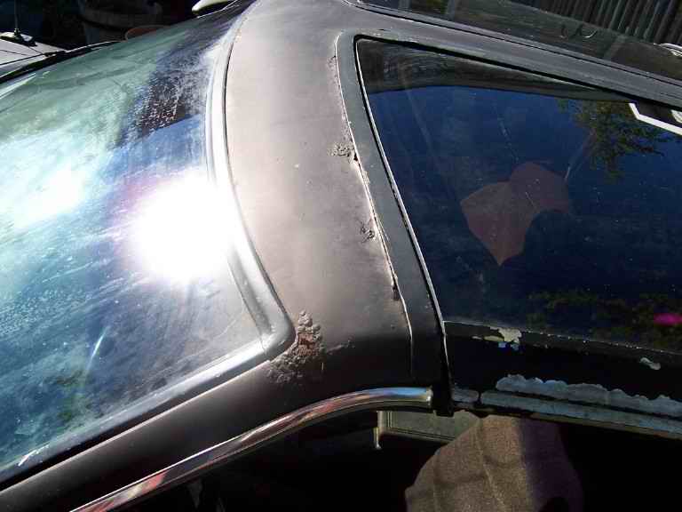 Close-up of a car's roofline showing rust on the trim near the windshield and side window