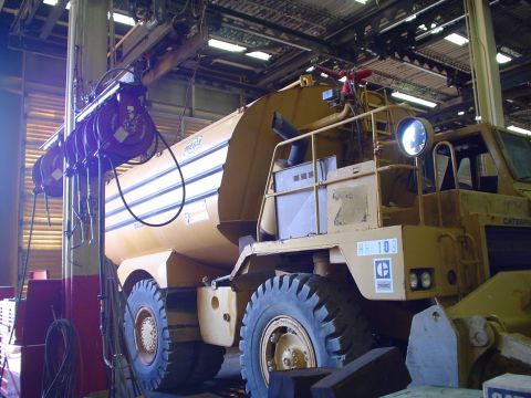 1966 International School Bus - A large yellow water truck is parked inside a workshop, with heavy-duty tires and a water tank visible.