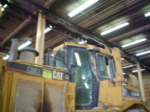 1966 International School Bus - A Caterpillar bulldozer is parked inside a building with a corrugated metal roof and fluorescent lighting.